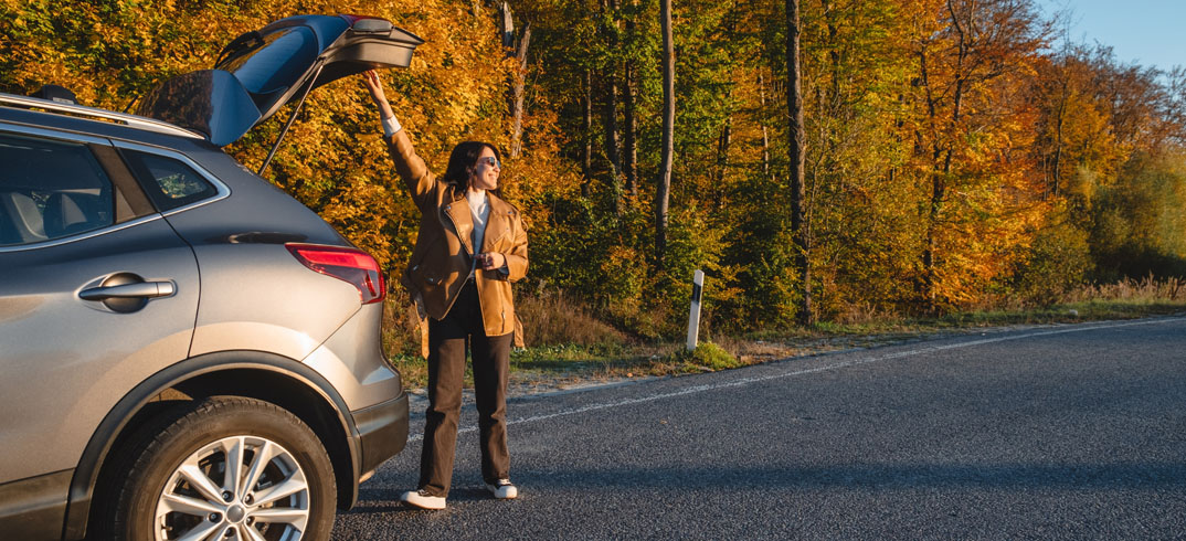 A woman stands beside her car with the trunk open, preparing to load or unload items