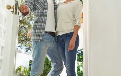 A smiling couple stands in a sunlit doorway, wearing casual jeans and tops
