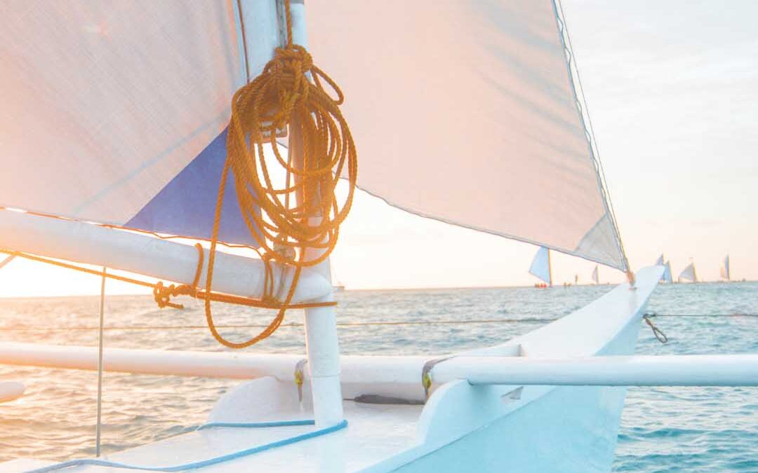 A sailboat gliding across the ocean, with gentle waves and a clear blue sky in the background.